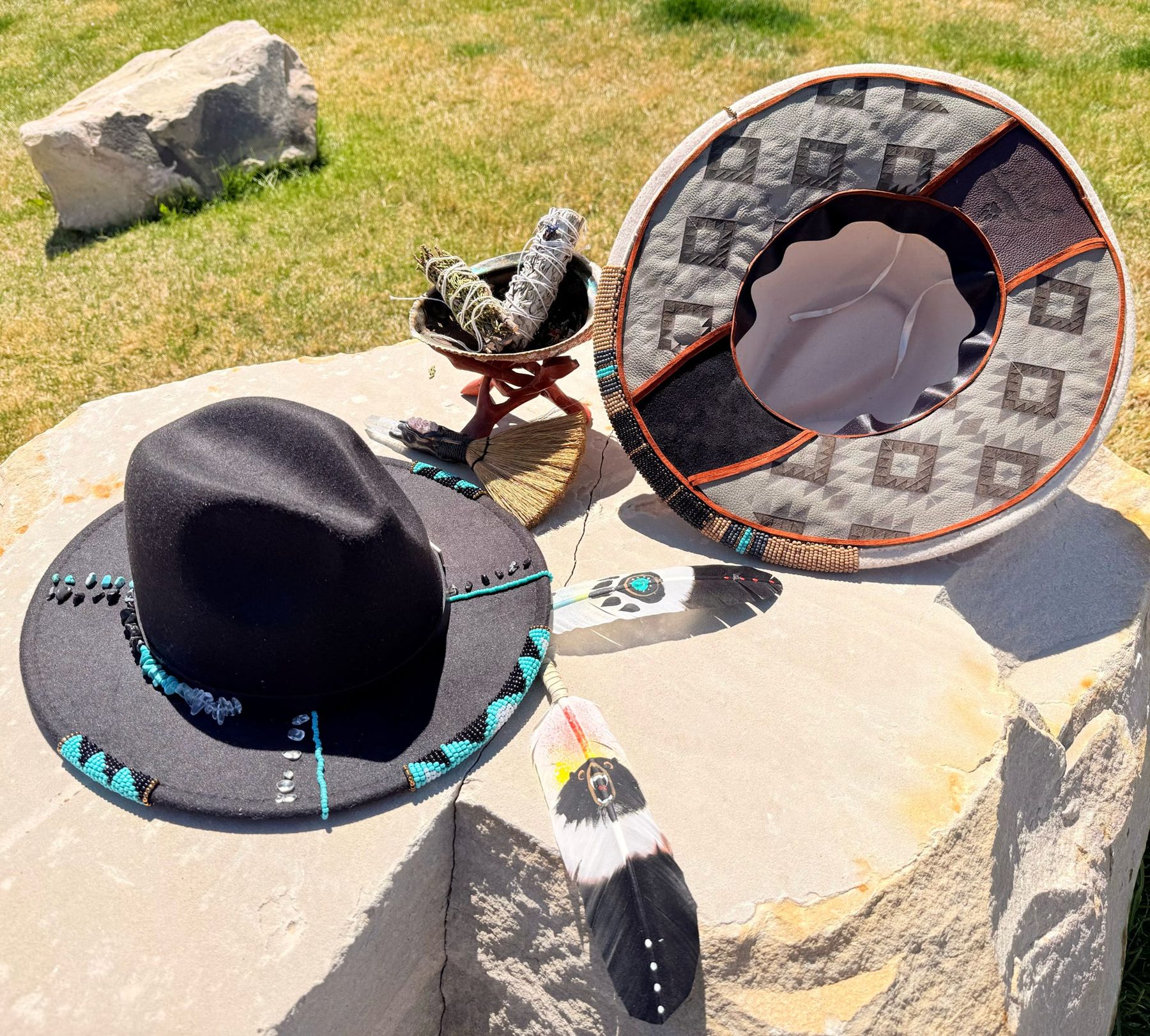 Two hand-beaded felt hats with turquoise beadwork, burned geometric brim detail and painted feathers, laid on sandstone